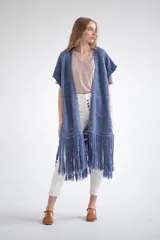 Chaleco largo de tejido de punto color azul, con mangas cortas y flecos largos en el ruedo. Presenta calados y bordados geométricos a lo largo de la prenda.