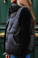 Chaleco puffer beige, sin mangas, con cuello alto, cierre frontal de cremallera y bolsillos laterales.