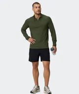 Remera deportiva de manga larga Fabletics modelo The Training Day, color verde militar, con cuello alto y cierre frontal parcial. Cuenta con tecnología antiolor y ojal para el pulgar en los puños.