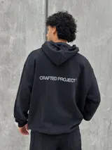 Canguro negro con capucha ajustable con cordones, bolsillo tipo canguro y estampado frontal con el texto "Crafted Project" y símbolos gráficos.