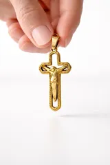 Dije religioso de acero dorado con forma de cruz calada y figura de Cristo en relieve en el centro.