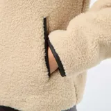 Campera de efecto borreguito en color beige, con cuello amplio y cierre frontal de botones negros. Presenta ribetes negros en contraste en el cuello, la apertura frontal y los puños. Marca Kiabi.