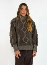 Sweater de punto color azul marino con cuello alto, diseño de rombos en relieve y detalles de flecos en las costuras de las mangas. Presenta un corte holgado con aberturas laterales en el ruedo.