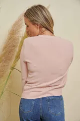 Saco de punto color rosado, con cuello redondo y cierre frontal abotonado. Presenta detalles de strass alrededor del cuello y en los botones.