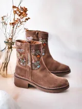 Botas de caña baja de cuero serraje color beige, con detalles de flores bordadas en los laterales. Poseen tacón ancho y cierre de cremallera lateral.