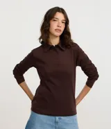 Blusa tipo polo de manga larga, confeccionada en tejido interlock de algodón y poliéster. Presenta cuello clásico con cierre frontal de botones y diseño básico liso.