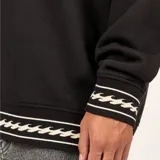Buzo de cuello redondo color negro, con diseño holgado y detalles de franjas con patrón de ondas en los puños y el ruedo. Presenta el logo de la marca bordado en el pecho.