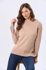 Buzo tejido de lana en color camel con cuello redondo alto, manga larga y terminaciones acanaladas en puños y cintura. Presenta tajos laterales y en los puños, además de una pequeña etiqueta de cuerina decorativa en el borde inferior.