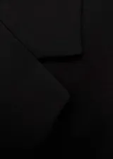 Abrigo largo estructurado de color negro con cuello de solapa, hombros marcados y cierre frontal de un botón. Presenta dos bolsillos laterales con solapa y forro interior.