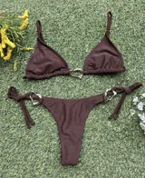 Conjunto de bikini color marrón chocolate, con corpiño triangular y bombacha colaless con tiras laterales para atar. Ambas piezas cuentan con argollas metálicas decorativas en el centro y los laterales.