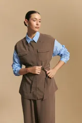 Chaleco negro de corte estructurado con cuello redondo, cierre frontal oculto y lazo ajustable en la cintura. Presenta dos bolsillos frontales con solapa y diseño de hombros caídos.