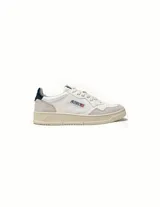 Championes de estilo vintage inspirados en los años 80, confeccionados en cuero blanco con detalles en gamuza gris. Presentan perforaciones en la puntera, cierre con cordones planos de algodón, cuello acolchado y parche trasero en color azul con logo en relieve. Incluyen suela de goma con logo y forro interior de cuero y rizo de algodón.