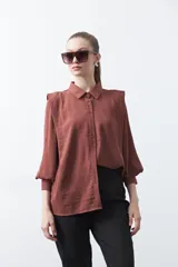 Camisa de vestir color marrón, con cuello clásico, mangas largas abullonadas y cierre frontal con botones.