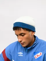 Gorro tipo beanie de punto acanalado en color azul marino, con vuelta en color rojo y blanco a rayas. Incluye etiqueta lateral con el logo de Umbro y el escudo del Club Nacional de Football.