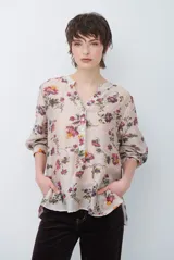 Camisa de corte holgado con estampado floral en tonos rojizos y verdes sobre base beige. Presenta cuello mao con escote en V, cierre frontal parcial con botones y mangas largas con puños ajustados.