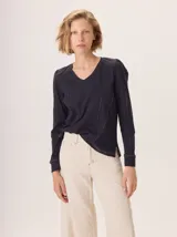 Remera blanca de manga larga con escote en V y detalles de alforzas verticales en el frente y mangas.