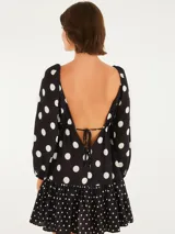 Vestido corto con estampado de lunares blancos sobre fondo negro, con escote profundo en V, mangas largas abullonadas y falda en capas con acabado en marias.