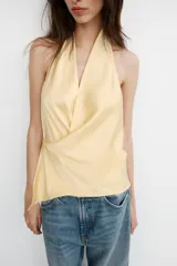 Top de tejido satinado con cuello halter y escote en pico cruzado. Presenta un diseño de espalda descubierta y bajo asimétrico con cierre lateral.
