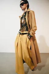 Jeans de tiro bajo y corte wide leg, color amarillo mostaza, con pliegues frontales, bolsillos ocultos y cierre frontal con cremallera, botón y ganchos metálicos.
