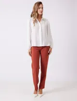 Camisa de gasa blanca con cuello solapa y cierre frontal de botones. Presenta un delicado galón de encaje festoneado a lo largo de la cartera frontal. Sus mangas largas son ligeramente abullonadas, con insertos de puntilla horizontal y puños elásticos fruncidos.