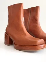 Bota de caña media color óxido, confeccionada en cuero, con plataforma y taco cuadrado texturizado, punta cuadrada y cierre lateral.