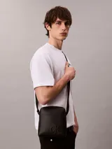 Bandolera reporter Calvin Klein de poliuretano color negro, con correa ajustable al hombro, cierre superior con cremallera, bolsillo frontal externo y logo monograma grabado en la parte inferior.