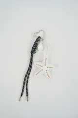 Llavero con mosquetón en forma de corazón, cordón negro trenzado, dije de caracol perlado y colgante de estrella blanca con tachas doradas.