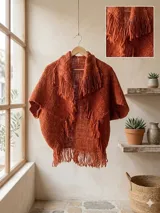 Capita tejida en lana merino pura color terracota, con mangas cortas amplias, solapa ancha y detalles de flecos en los bordes.