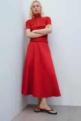 Falda midi de tiro alto y corte en A, color rojo, con bolsillos laterales ocultos y cierre lateral con cremallera.
