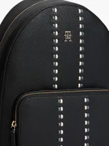 Mochila de diseño minimalista con acabado granulado, confeccionada en poliuretano. Presenta un compartimento principal con cierre de cremallera, un bolsillo exterior frontal con cierre, asa superior y correas ajustables. Incluye un detalle de cinta distintiva tonal en la parte delantera y el monograma TH metálico.