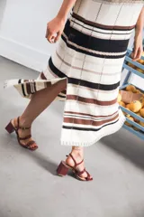 Vestido largo de tejido calado con rayas horizontales en tonos beige, marrón y amarillo. Tiene corte recto, hombros caídos, tajo lateral y logo bordado en la manga.