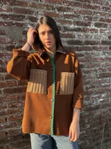 Camisa marrón con cuello, cierre frontal con botones, dos bolsillos frontales y detalles de lentejuelas.