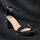 Sandalia de tacón cuadrado medio, color negro, con acabado brillante tipo glitter. Presenta una tira frontal ancha y una tira ajustable al tobillo con hebilla metálica dorada.