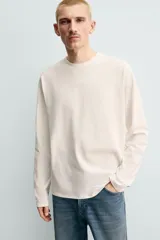 Camiseta de manga larga con corte relajado, confeccionada en tejido de algodón compacto. Presenta cuello redondo y detalle de costura en el centro de la espalda.
