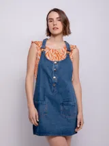 Jumper de jean azul con tiras regulables, cuatro botones metálicos, hebillas y dos bolsillos delanteros.