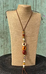 Colgante largo de cordón de cuero con cuentas decorativas de madera, resina y metal en tonos marrones, amarillos y naranjas.