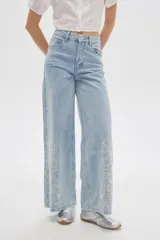 Pantalón jean de tiro alto y corte ancho, color celeste, con delicados bordados de flores blancas en la parte inferior de las piernas.