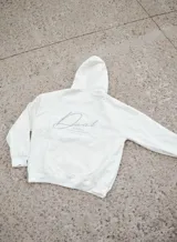 Hoodie canguro blanco de diseño oversize, con capucha, bolsillo frontal tipo koozban y sutil bordado monocromático en el pecho.