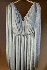 Vestido largo plisado color plateado, con escote en V, mangas largas y un cinturón trenzado con brillos en la cintura.