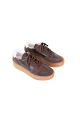 Championes de plataforma con diseño deportivo, confeccionados en una combinación de cuero y gamuza en tonos marrón oscuro. Presentan suela de goma color caramelo y detalles en color crema en la parte trasera.
