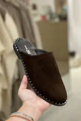 Zuecos de gamuza color marrón chocolate con suela plana y detalle de tachas pequeñas alrededor de la suela.