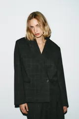 Blazer corto de corte oversize con estampado de cuadros, cuello con solapas de muesca y manga larga. Presenta cierre frontal cruzado con un botón y falsos bolsillos de vivo en el delantero. Incluye forro interior.