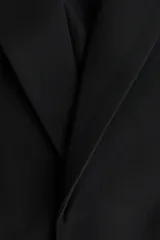 Blazer de sarga con solapas de pico, diseño de frente abierto y bolsillos delanteros ribeteados con solapa. Presenta mangas diseñadas para ser remangadas, dejando a la vista un forro interior a rayas.