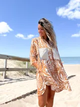 Camisero corto de manga tres cuartos, con cuello camisero y botones frontales. Presenta un estampado botánico en tonos marrón óxido y blanco, con dos bolsillos cuadrados de color beige liso en el pecho.