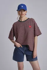 Remera oversize a rayas horizontales en tonos bordó y blanco, con cuello redondo verde oscuro y un pequeño parche bordado en forma de corazón en el pecho.