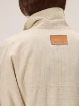 Chaquetas de lino bicolor en tonos blanco y beige, con diseño holgado, cuello alto, cierre frontal de botones, bolsillos con solapa en el pecho y mangas cortas con presilla y botón.