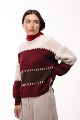 Sweater de tejido de punto grueso con diseño de bloques de color en tonos beige, marrón y bordó. Presenta un corte relajado, mangas amplias y detalles de costuras visibles en contraste que separan las franjas de color.