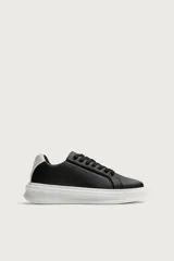 Zapatilla deportiva de diseño minimalista, confeccionada en material sintético negro con suela de plataforma blanca y detalle de contraste en el talón.
