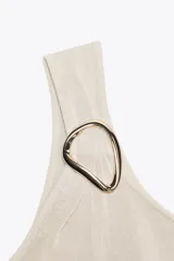 Top blanco de punto con escote asimétrico y aplique metálico dorado en el hombro.