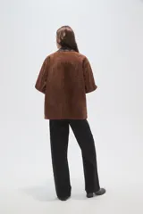 Chaqueta de gamuza color marrón con cuello camisero en cuero oscuro, cierre frontal con broches metálicos tipo gancho y bolsillos delanteros aplicados.